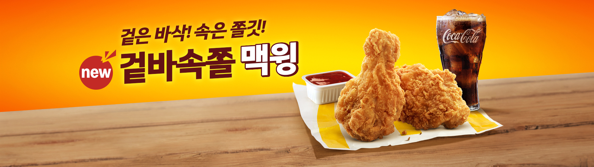 노란색 그라데이션 배경 위에 나무 테이블이 놓여 있고, 테이블 위에는 치킨 윙 두 조각이 노란 종이 포장지 위에 놓여 있으며, 옆에는 사각 흰색 소스 용기에 붉은색 소스가 담겨 있으며, 오른쪽에는 얼음이 들어간 콜라가 함께 배치되어 있다. 좌측 상단에는 ‘겉은 바삭! 속은 촉촉!’ 문구와 함께 new 배지가 붙은 겉바속촉 맥윙 제품명이 크게 노출된 맥도날드 배너 이미지