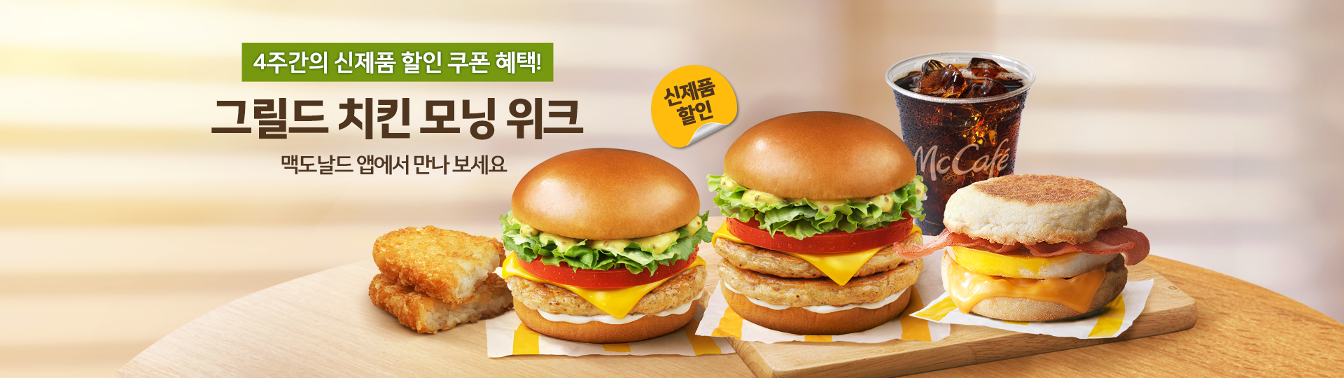 맥도날드 앱에서 제공하는 그릴드 치킨 모닝 위크 신제품 할인 쿠폰 혜택 안내 배너.  “4주간의 신제품 할인 쿠폰 혜택!”, “그릴드 치킨 모닝 위크”, “맥도날드 앱에서 만나 보세요” 문구와 “신제품 할인” 배지가 표시되어 있으며,  해시브라운, 그릴드 치킨 모닝 버거, 더블 그릴드 치킨 모닝 버거, 아이스 커피, 베이컨 에그 맥머핀이 나무 보드 위에 함께 배치되어 있다.
